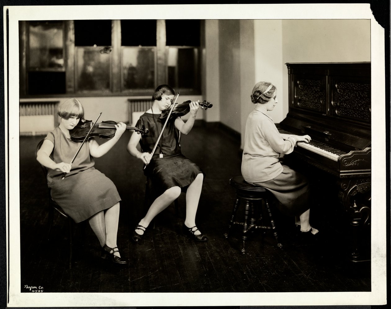 Grupp om tre unga blinda kvinnor, en vid pianot, två spelar fioler, på New York Association for the Blind, 111 East 59th Street, New York, 1926 (silvergelatintryck) av Byron Company