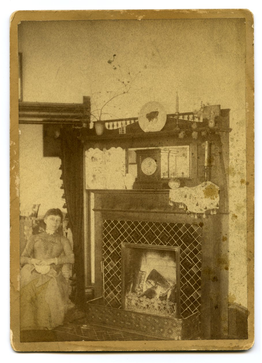 Woman seated beside a lit fireplace av Unknown