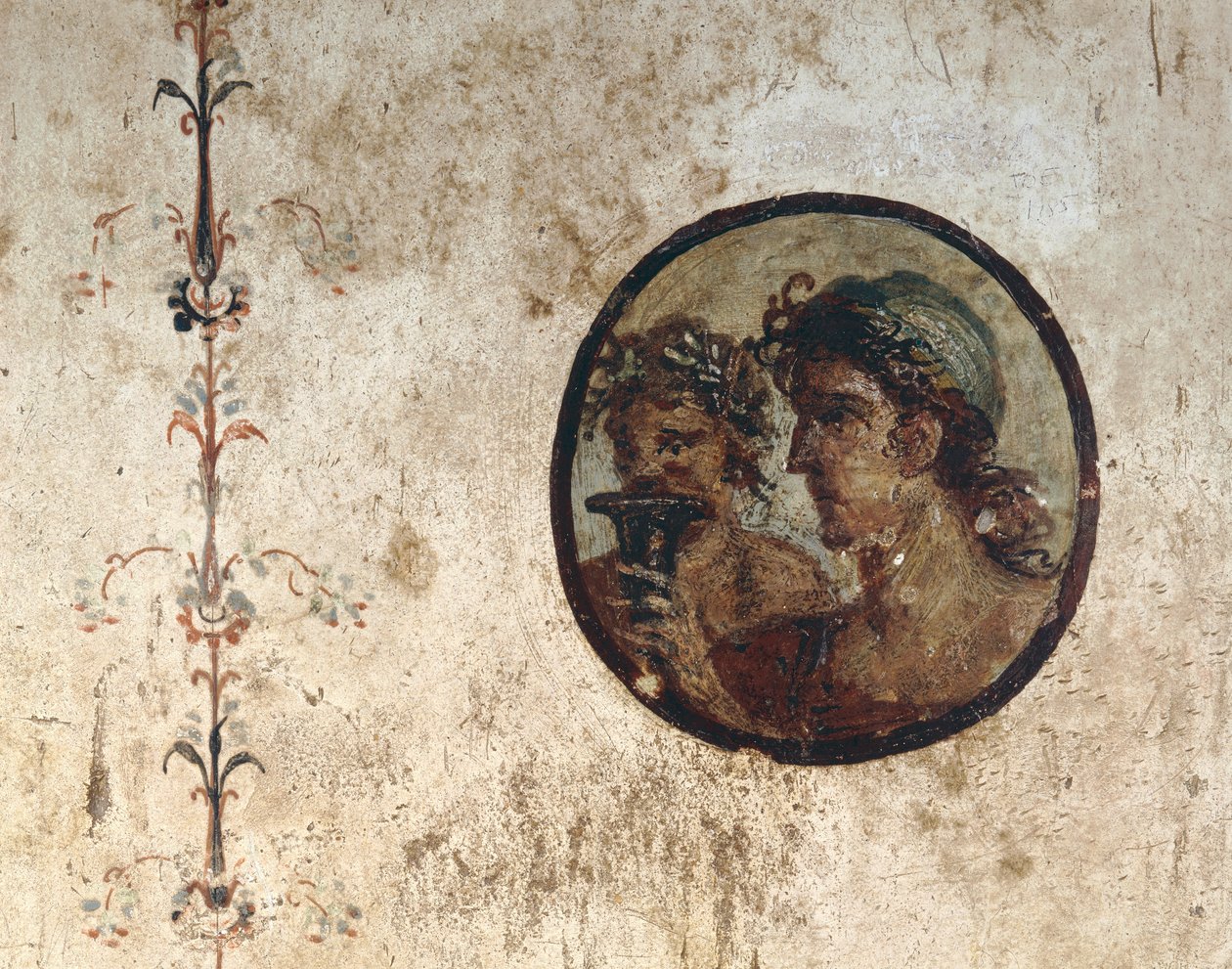 Interiör av ett rum med väggfresker från den romerska perioden, stil III, i huset Corieo Tiburtino i Pompeji: del av en vinstock och en tondo med två manliga huvuden av Unknown