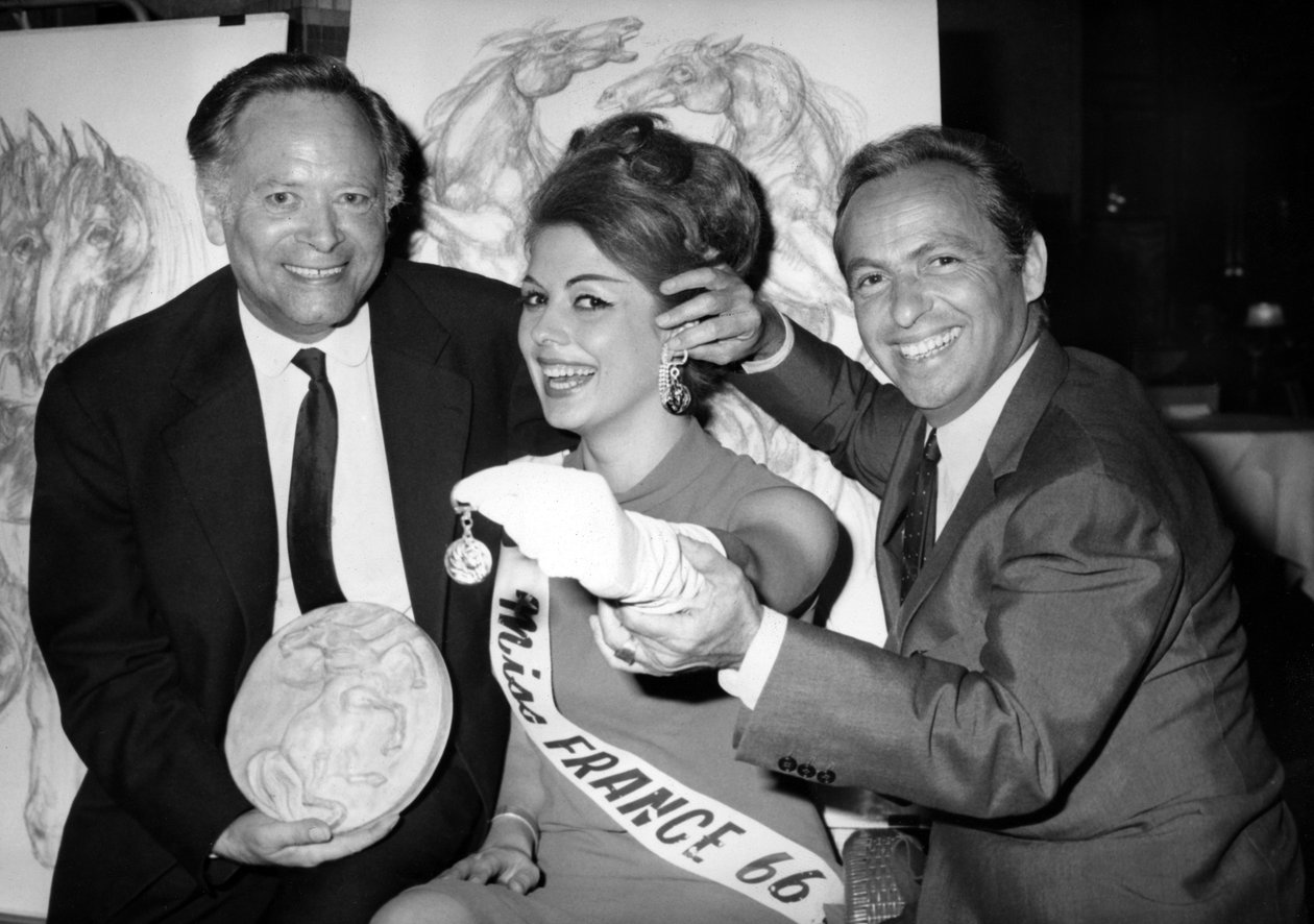 Rene Bollinger (vänster) och Guy Lux Entourent Monique Boucher "Miss France" till vem de precis lämnar in en nyckelring "Talisman Du Turfiste" under öppningen av Bollingers Canvas den 12 juli 1966 av Unknown