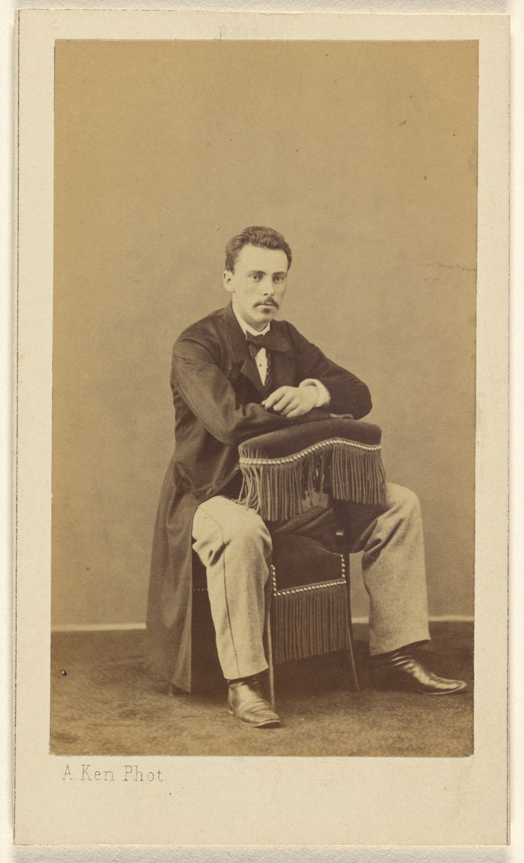[Man med mustasch, sittande, med framsidan mot baksidan av en stol med fransar] av Alexandre Ken