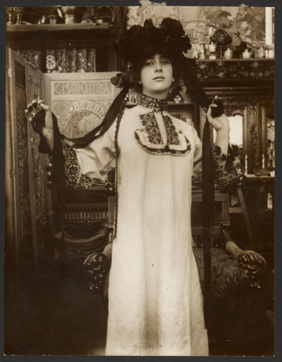 [Kvinnlig modell i lång vit dräkt och hatt med band, Paris] av Alphonse Maria Mucha