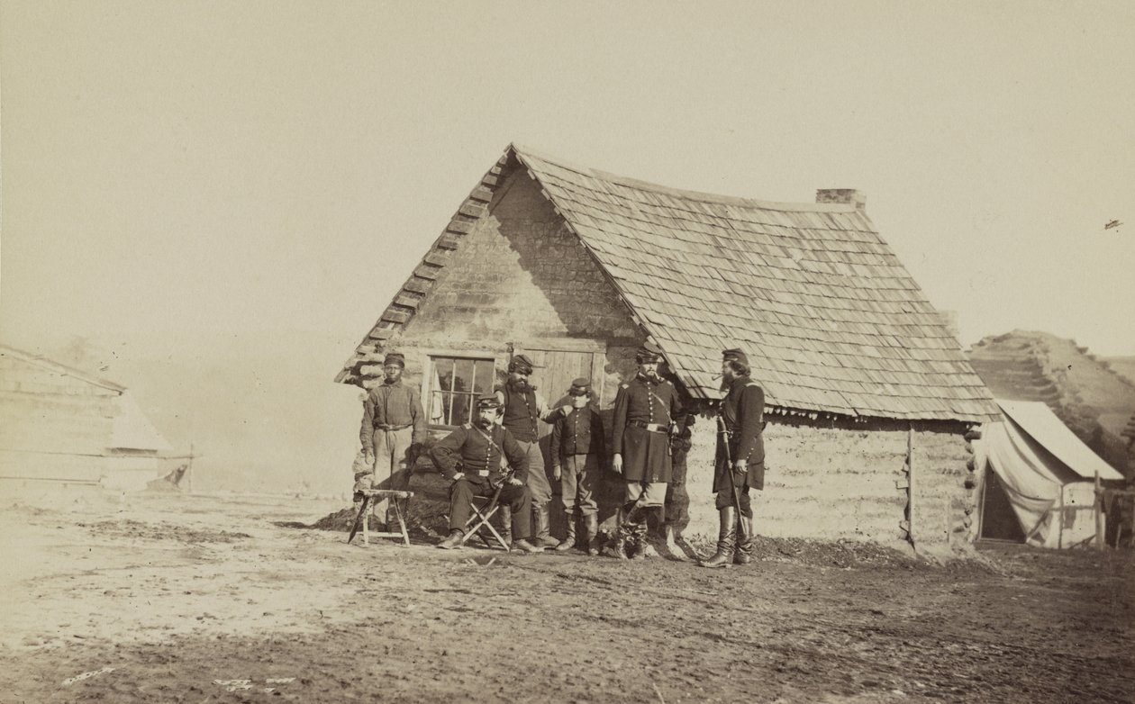 En grupp soldater och två unga män, en afroamerikan, står utanför timmerstugekvarteren, 1861-65 av American Photographer