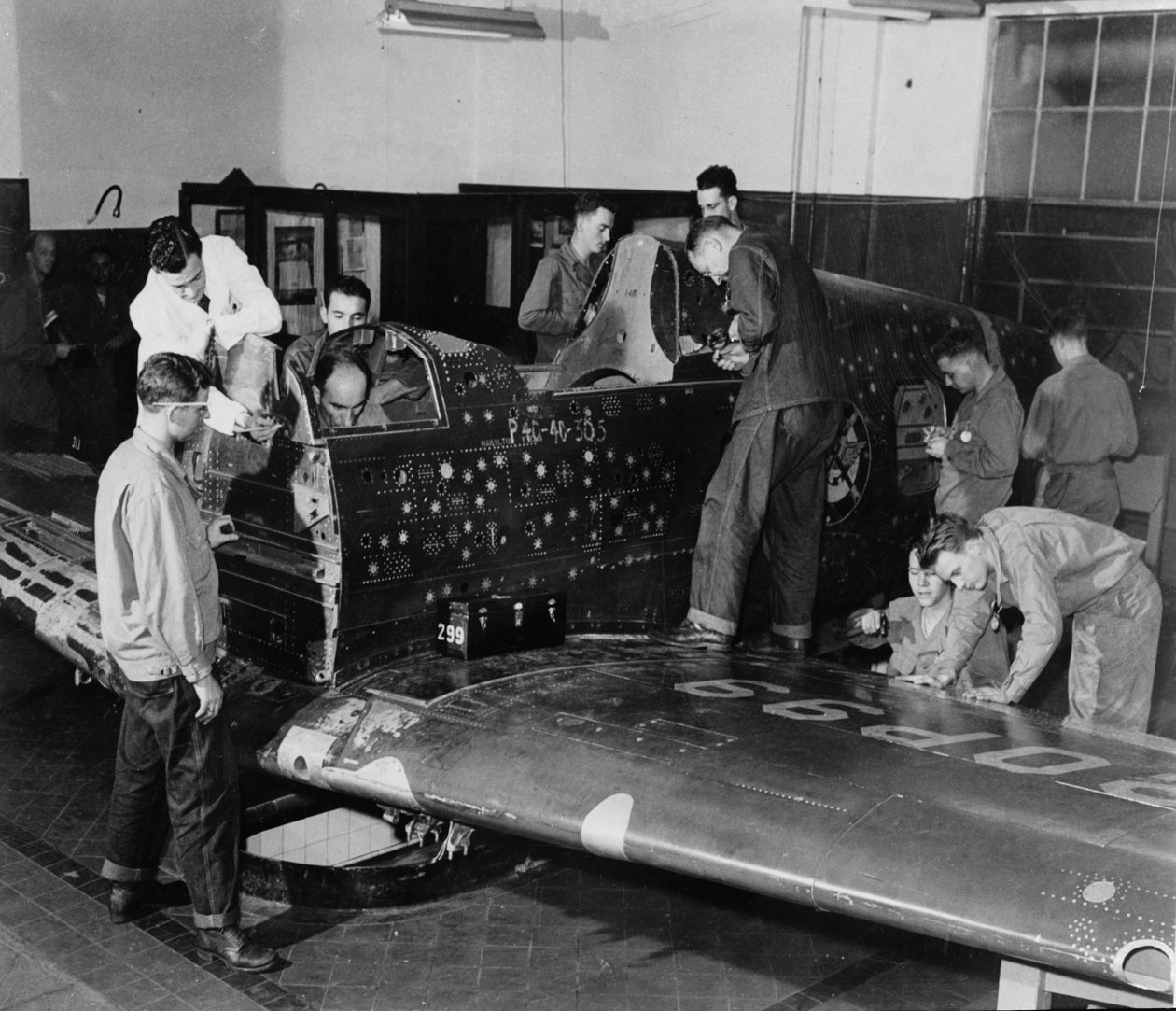 Soldatpraktikanter arbetar på "Flying Patch", ett Curtiss "Warhawk" stridsflygplan utan motor eller stjärtmontering, med simulerade skotthål och lappar, ca 1942 av American Photographer