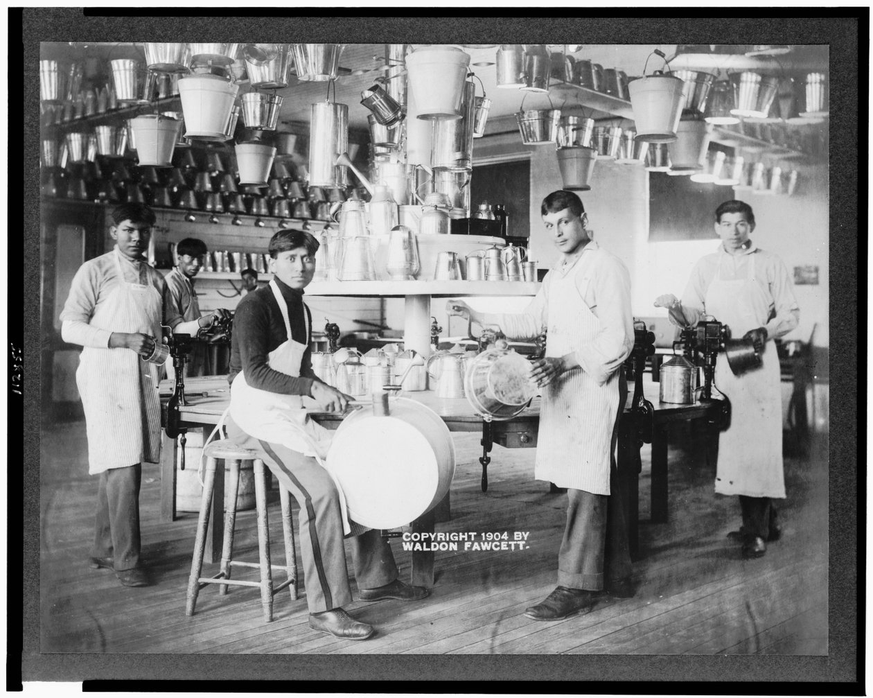Unga indianmän i metallbearbetningsverkstad med hinkar, tvättbaljor, vattenkannor och andra metallföremål, Carlisle Indian School, Pennsylvania, ca 1904 (s/v foto) av American Photographer