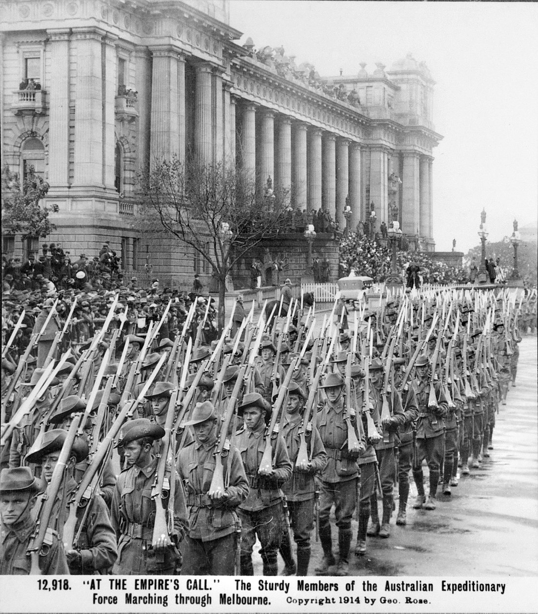 Män från AIF marscherar förbi parlamentsbyggnaden i Melbourne, Vic, med sina gevär med påsatta bajonetter över axlarna, före avfärd för utlandstjänstgöring, ca augusti 1914 av Australian Photographer