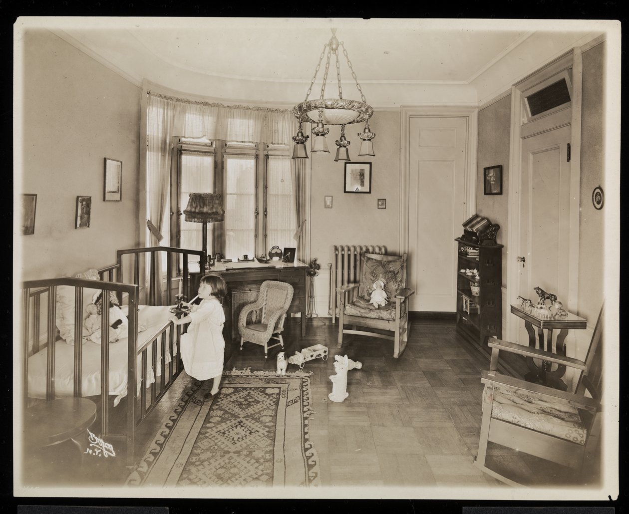 En flicka som håller ett ljus och klättrar upp i en spjälsäng i ett sovrum i A.C. Cronins bostad, 1915-16 (silvergelatinprint) av Byron Company