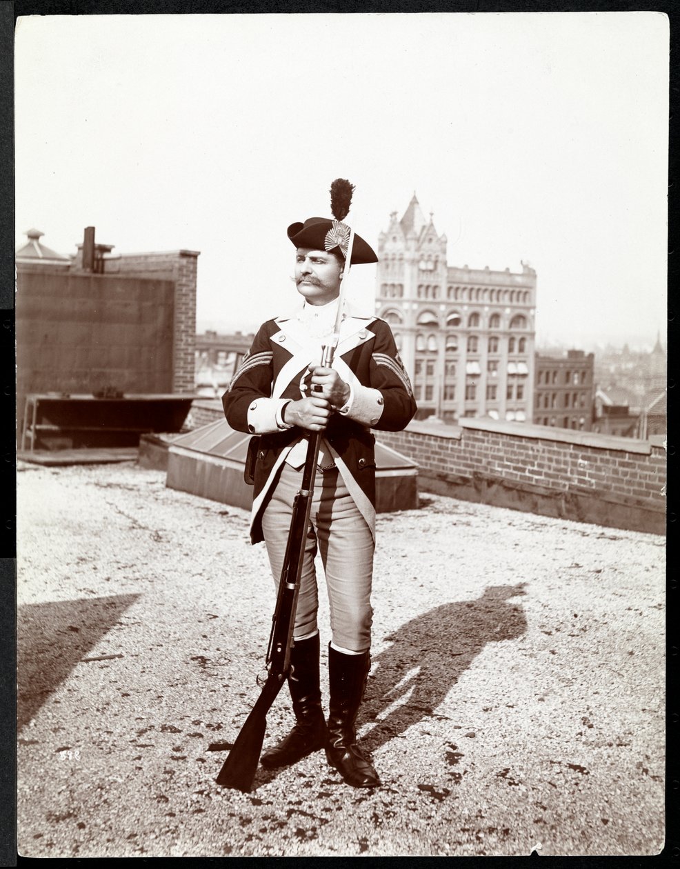 En man på ett hustak klädd i traditionell militäruniform med ett gevär i handen, 1895 (silvergelatintryck) av Byron Company