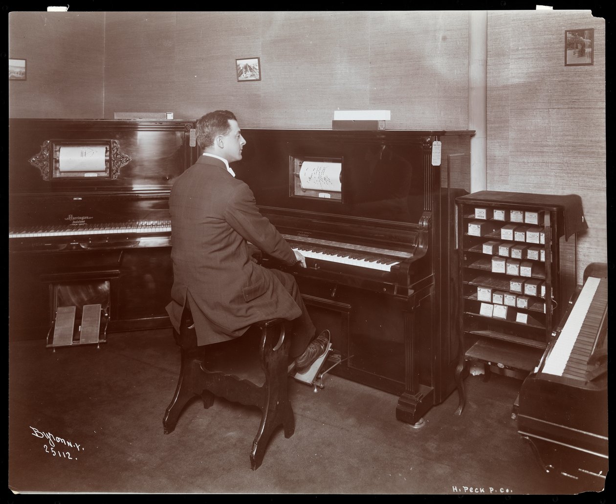 En man som spelar piano i ett pianoshowroom i New York, 1907 (silvergelatintryck) av Byron Company