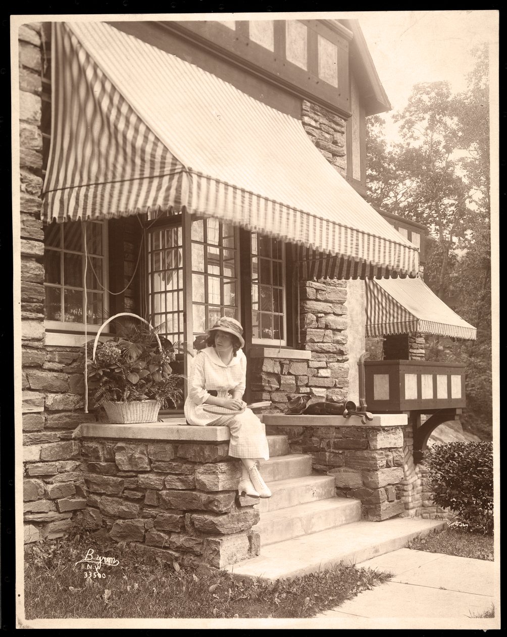 En kvinna som sitter vid ingången till ett hus, 1915 (silvergelatintryck) av Byron Company