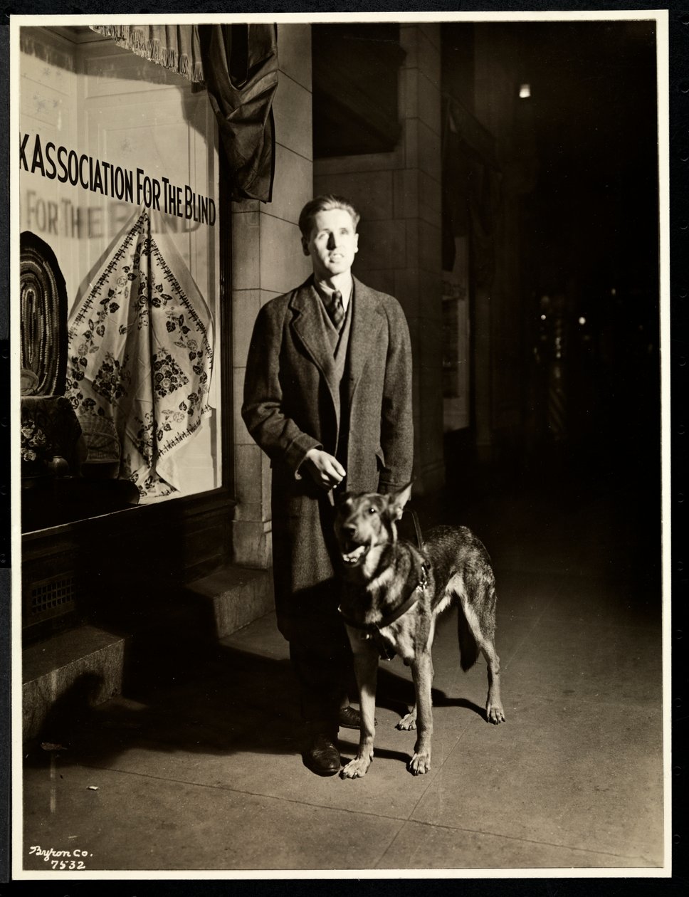 Blind man och hans ledarhund på trottoaren framför New York Association for the Blind, 111 East 59th Street, New York, 1938 (silvergelatintryck) av Byron Company