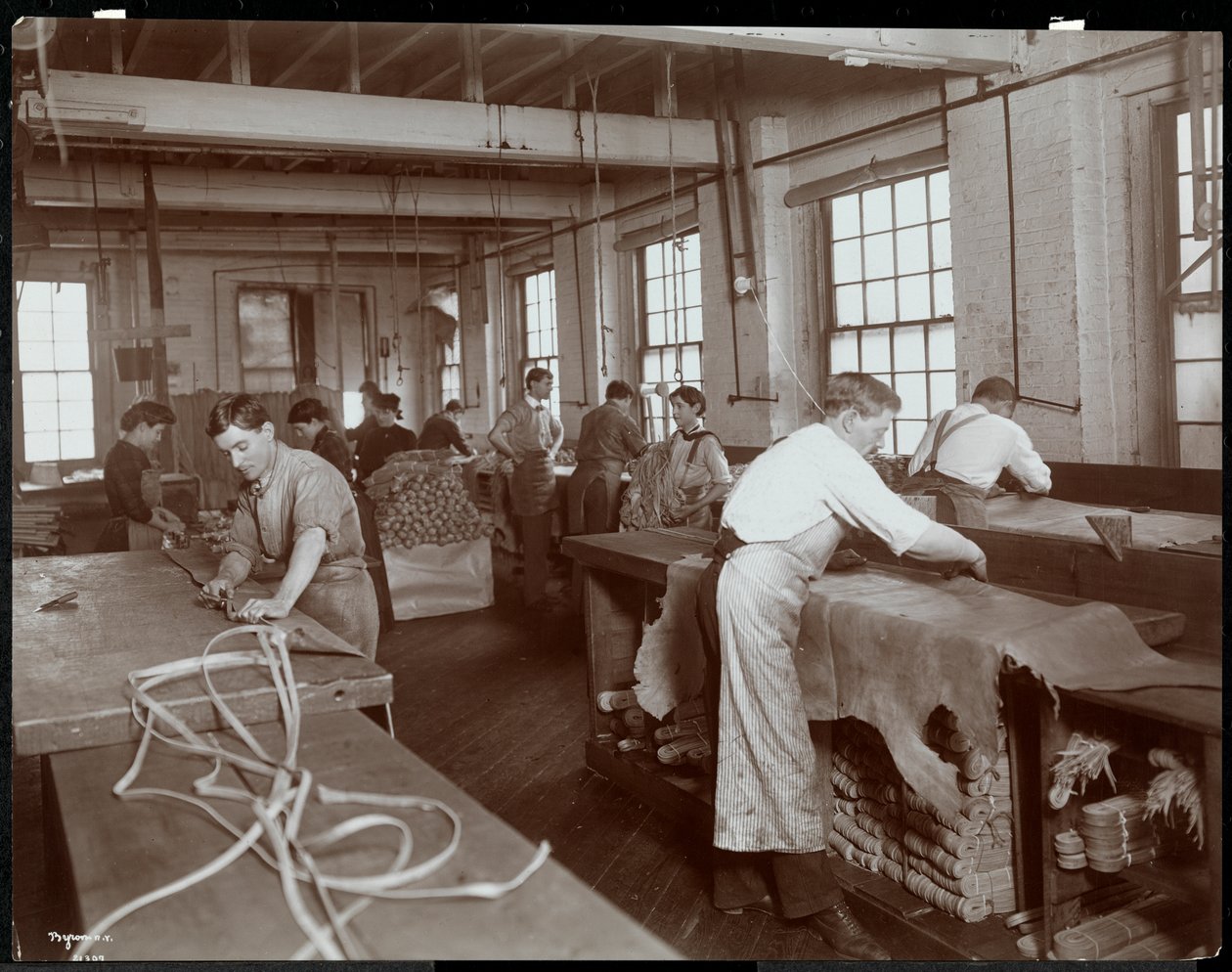 Interiörvy av män och kvinnor som arbetar med läder på New York Leather Belting Co., New York, 1906 (silvergelatintryck) av Byron Company