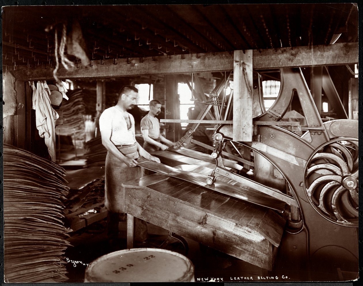 Interiör av två män som arbetar med läder och tung utrustning på New York Leather Belting Co. i New York, 1905 (silvergelatintryck). av Byron Company