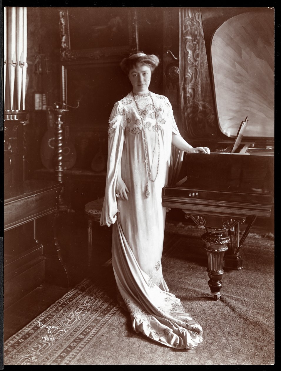 Porträtt av Mrs. I. M. Clark stående vid ett piano, 1904 (silvergelatintryck) av Byron Company