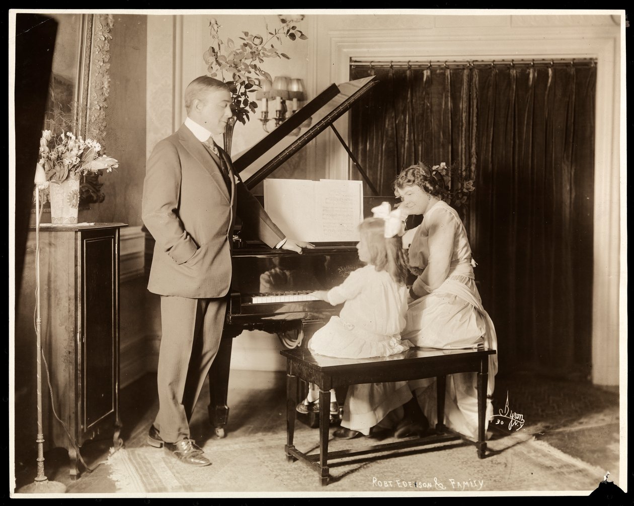 Robert Edeson, hans hustru och dotter vid pianot, ca 1915 (silvergelatintryck) av Byron Company