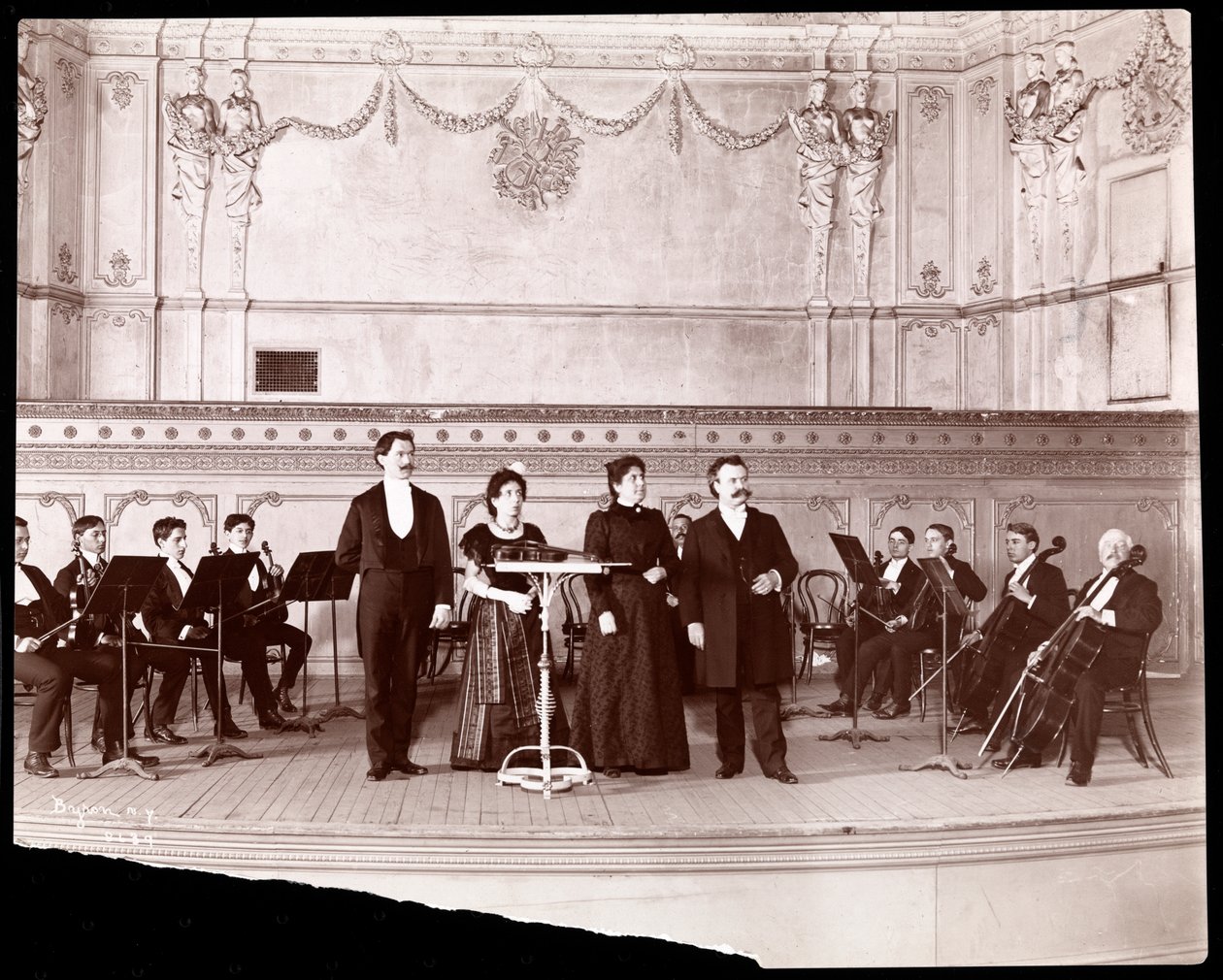 Stråksektion bakom manliga och kvinnliga sångare, 1905 (silvergelatintryck) av Byron Company