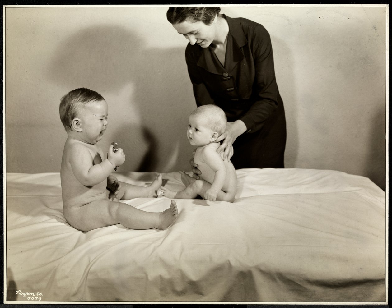 Två bebisar som sitter upp i sängen, den ena får stöd av en sjuksköterska, den andra håller i en leksaksbil och gråter på Maternity Center Association på 70th Street East River, New York, 1935 (silvergelatintryck av Byron Company