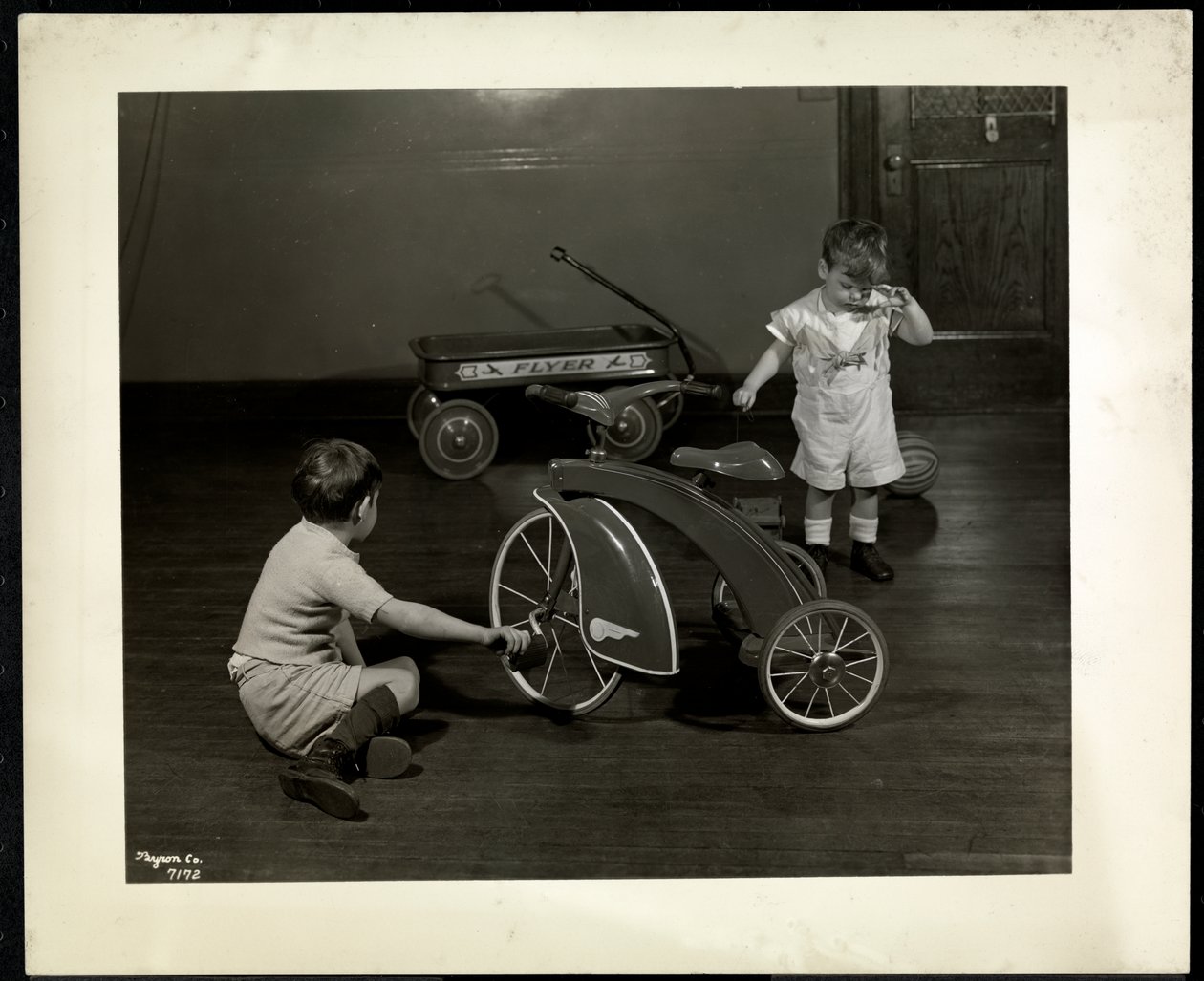 Två blinda synskadade pojkar som leker med en trehjuling och röd vagn på New York Association for the Blind, 111 East 59th Street, New York, 1937 (silvergelatintryck) av Byron Company