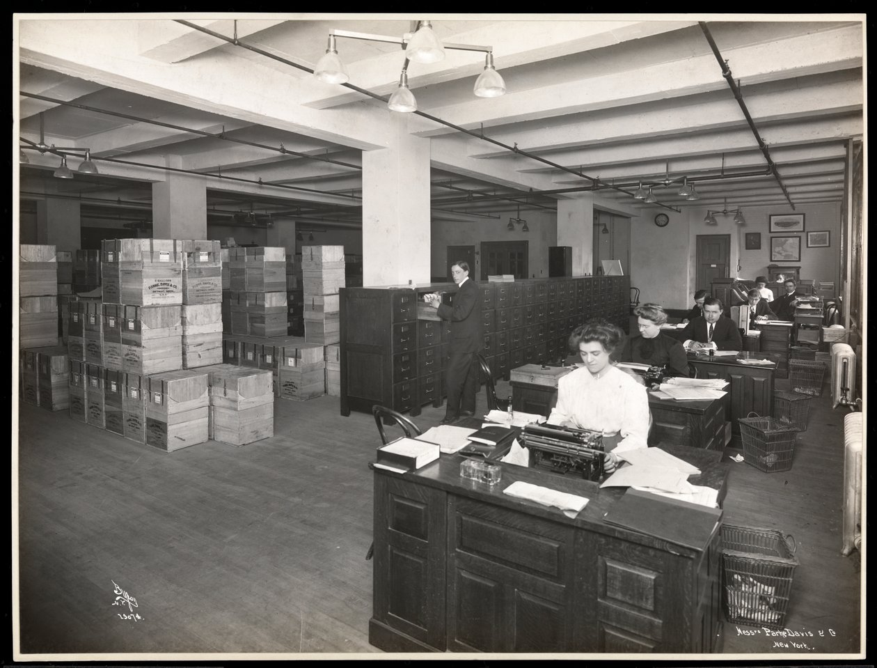 Vy över män och kvinnor vid skrivbord i vad som verkar vara ett expeditionsrum hos Parke, Davis och Co, kemister, Hudson och Vestry Streets, New York, 1910 (silvergelatintryck) av Byron Company