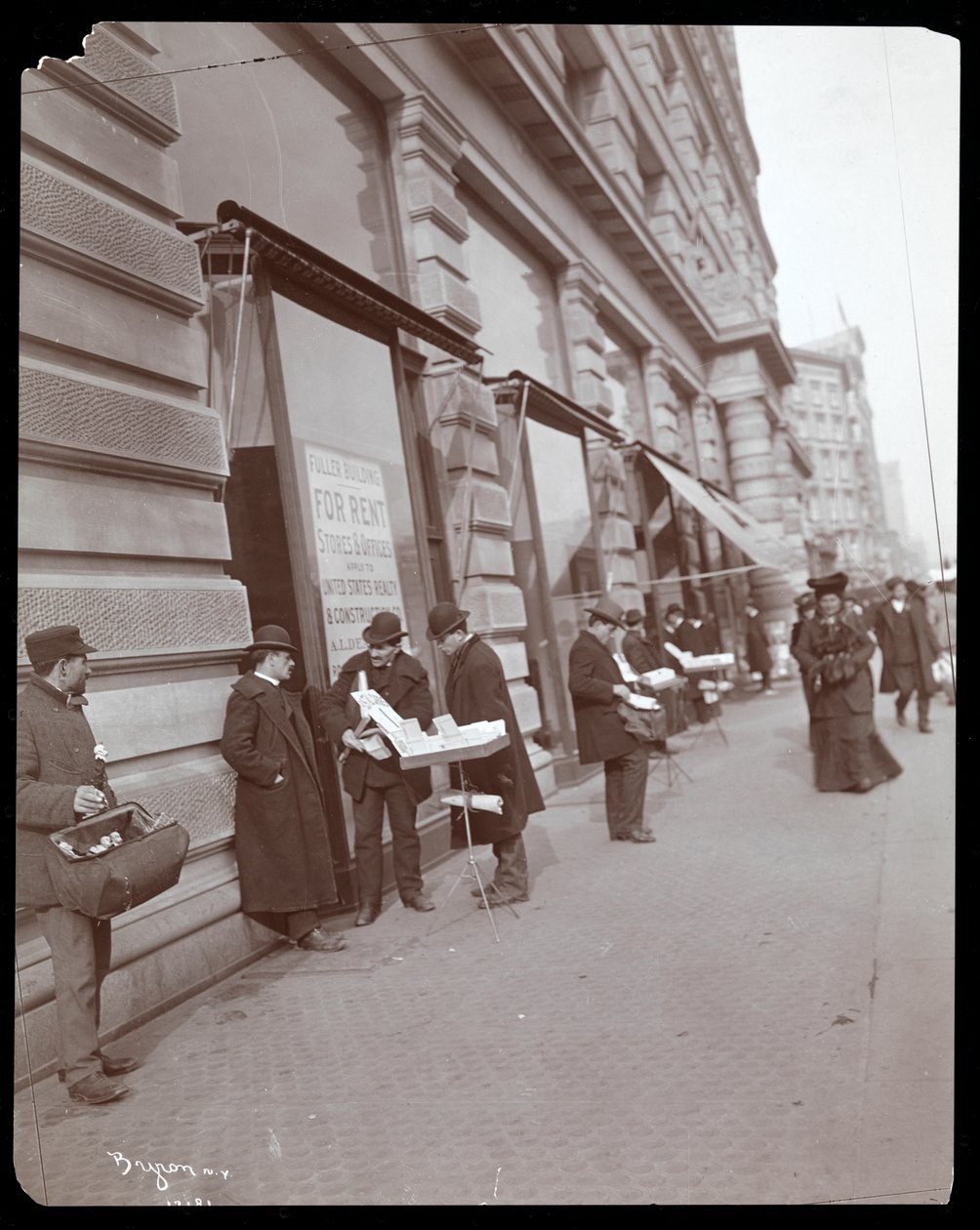 Vy över handlare som säljer leksaker och andra föremål framför Fuller eller Flatiron Building på Broadway, 5th Avenue och 23rd Street, New York, ca 1895 (silvergelatintryck) av Byron Company