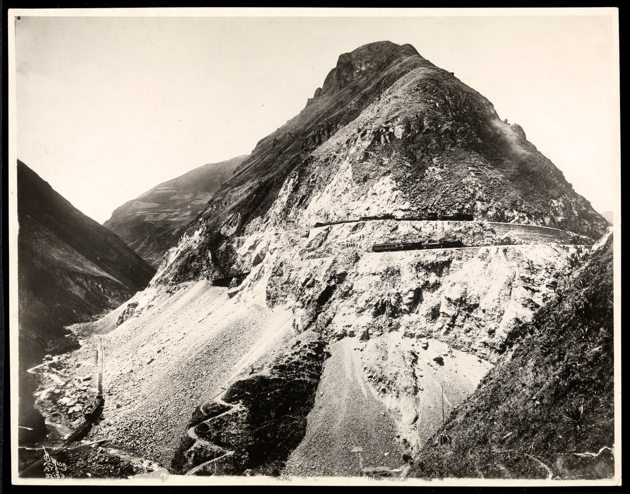 Vy över två järnvägståg på spår längs ett berg, förmodligen på eller nära Panamakanalen, 1912 eller 1913 (silvergelatintryck) av Byron Company