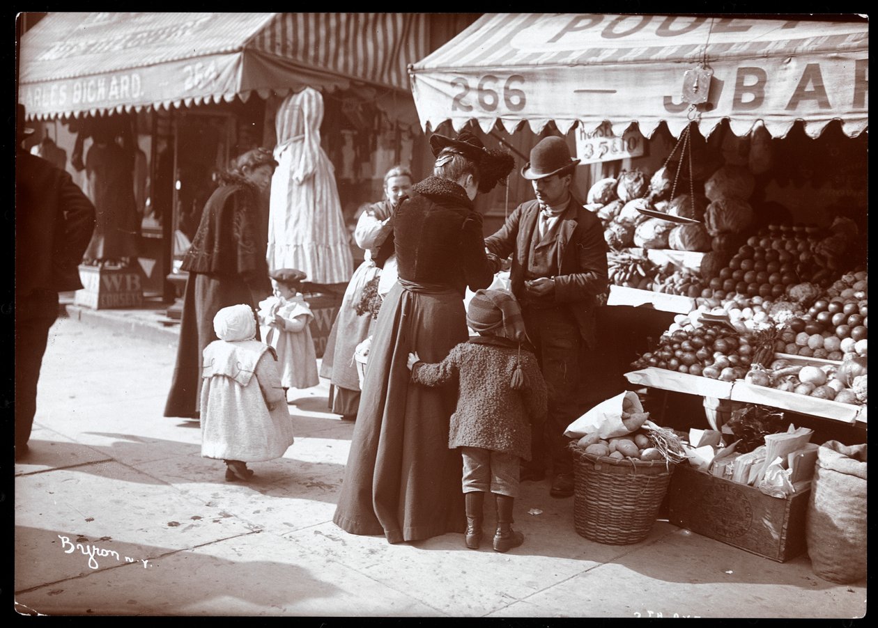 Vy över kvinnor med barn som shoppar vid ett frukt- och grönsaksställ på 266 7th Avenue, New York, ca 1900 (silvergelatintryck) av Byron Company