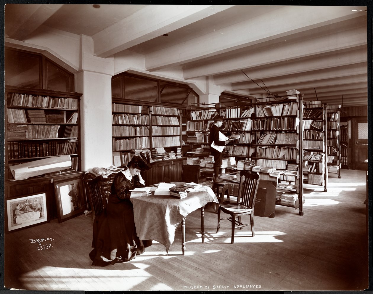 Kvinna och en ung man i ett bibliotek i Museum of Safety Appliances vid American Institute of Social Service, New York, 1907 (silvergelatintryck) av Byron Company