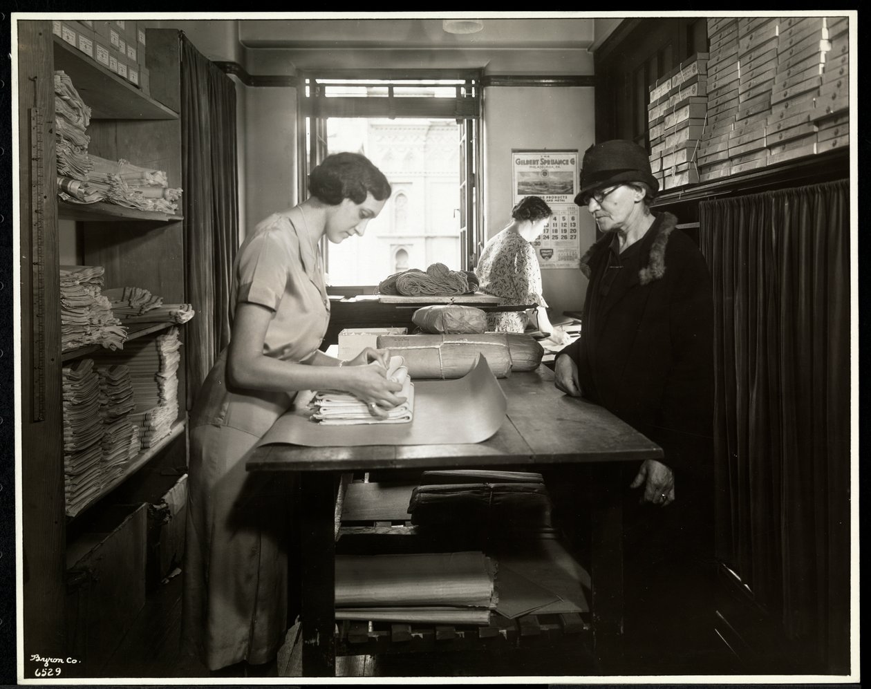 Ung kvinna slår in tygmaterial som en hemarbetare kan ta med sig, på New York Association for the Blind, 111 East 59th Street, New York, 1931 (silvergelatintryck) av Byron Company