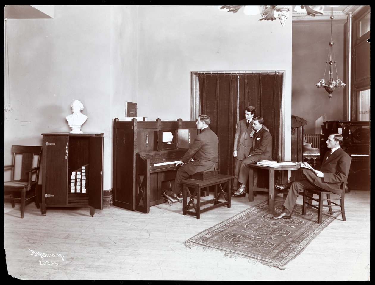 Fyra män, varav en spelar ett piano från H. Bruman Co., 1907 (silvergelatintryck) av Byron Company