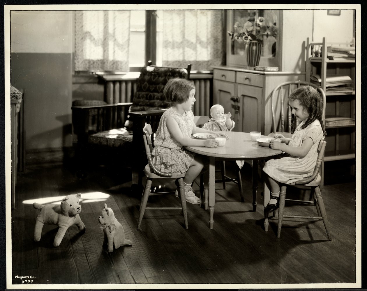Två blinda synskadade flickor äter vid ett litet bord med en docka på New York Association for the Blind, 111 East 59th Street, New York, 1933 (silvergelatintryck) av Byron Company