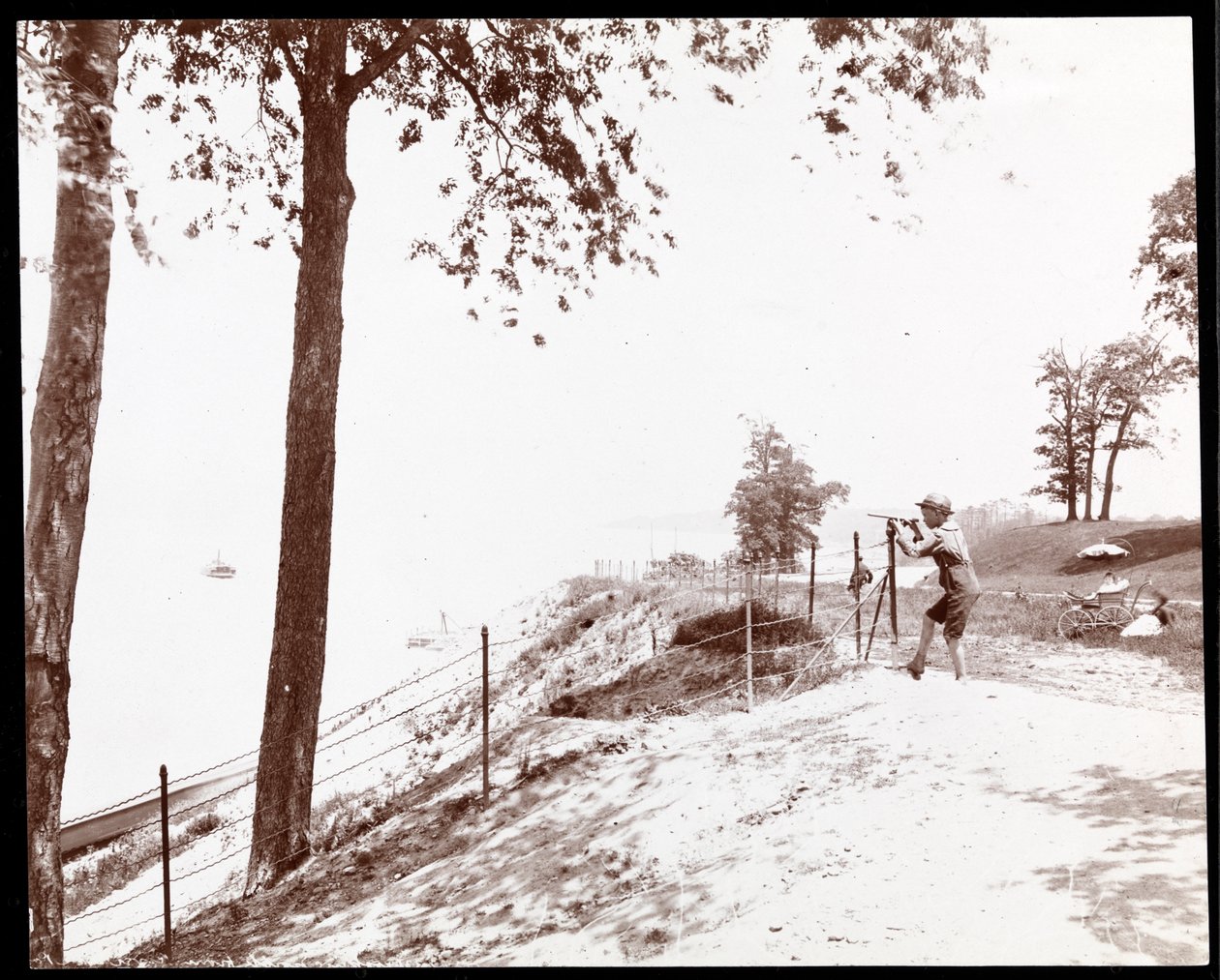Vy över en pojke med ett kikare som tittar mot Hudsonfloden från Riverside Park, New York (silvergelatintryck) av Byron Company