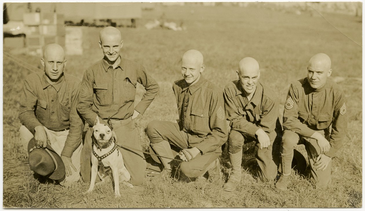 Fem soldater knäböjer i gräset och poserar för en bild med en hund i koppel av Carl Michel