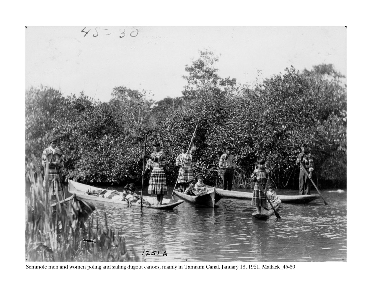 Seminole män och kvinnor som polar och seglar utgravda kanoter på Tamiami Canal, 18 januari 1921 av Claude C. Matlack