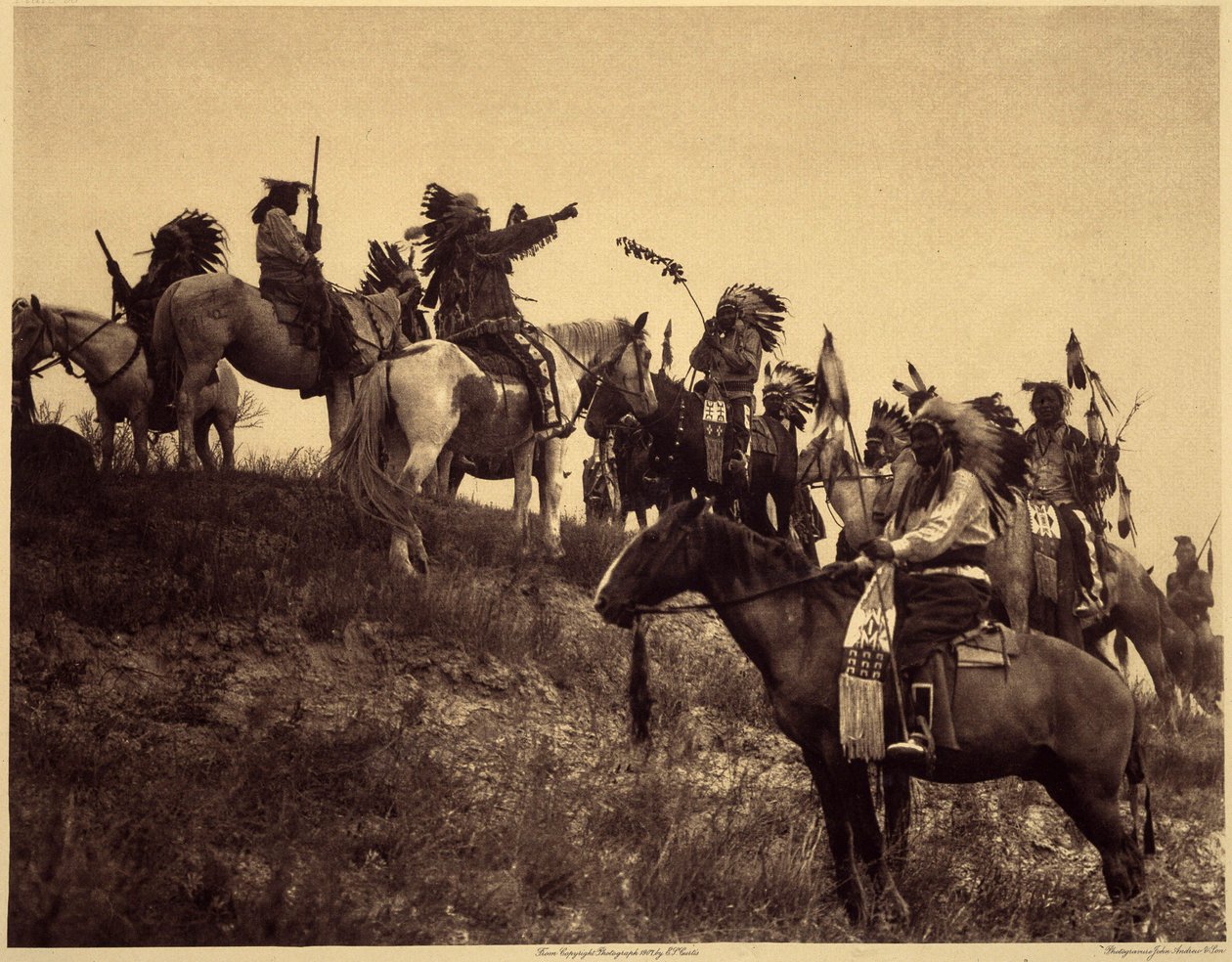 Planerar en razzia. Indianerna, i sina imponerande typiska dräkter, samlas i extremt pittoreska grupper. Det här är en trupp från Sioux Ogalala (Oglala), på en kulle med utsikt över Wounded Knee Valley i Pine Ridge Reserve, South Dakota. Foto tak av Edward Sheriff Curtis