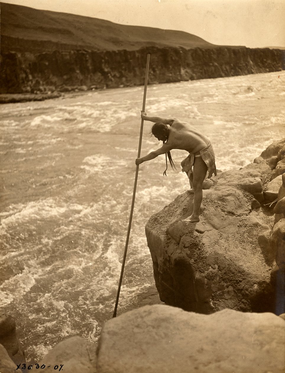 Tlakluit-indian, stående på klippa, fiskar med håv, ca 1910 (svartvitt foto) av Edward Sheriff Curtis