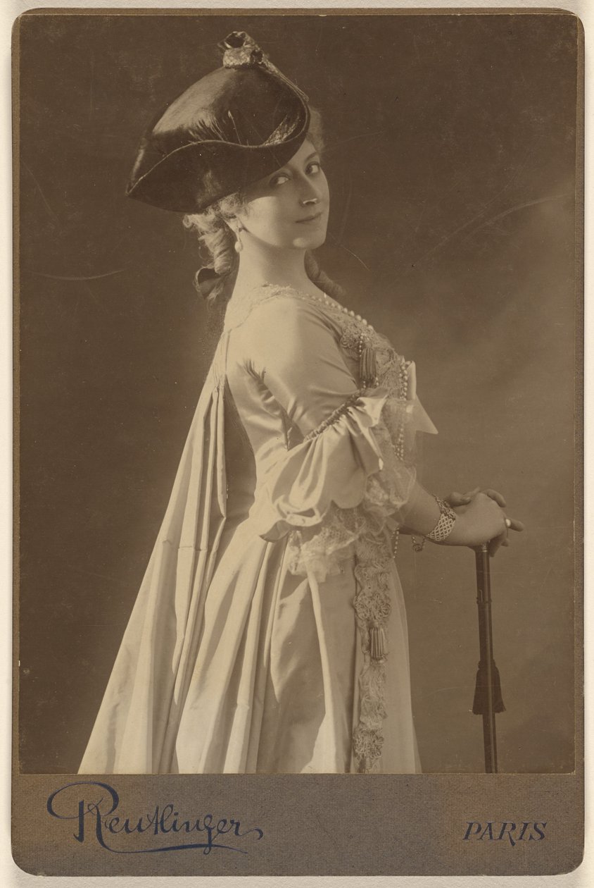 [Oidentifierad kvinna med mörk hatt, stående, med händerna vilande på en käpp] av Emile Auguste Reutlinger