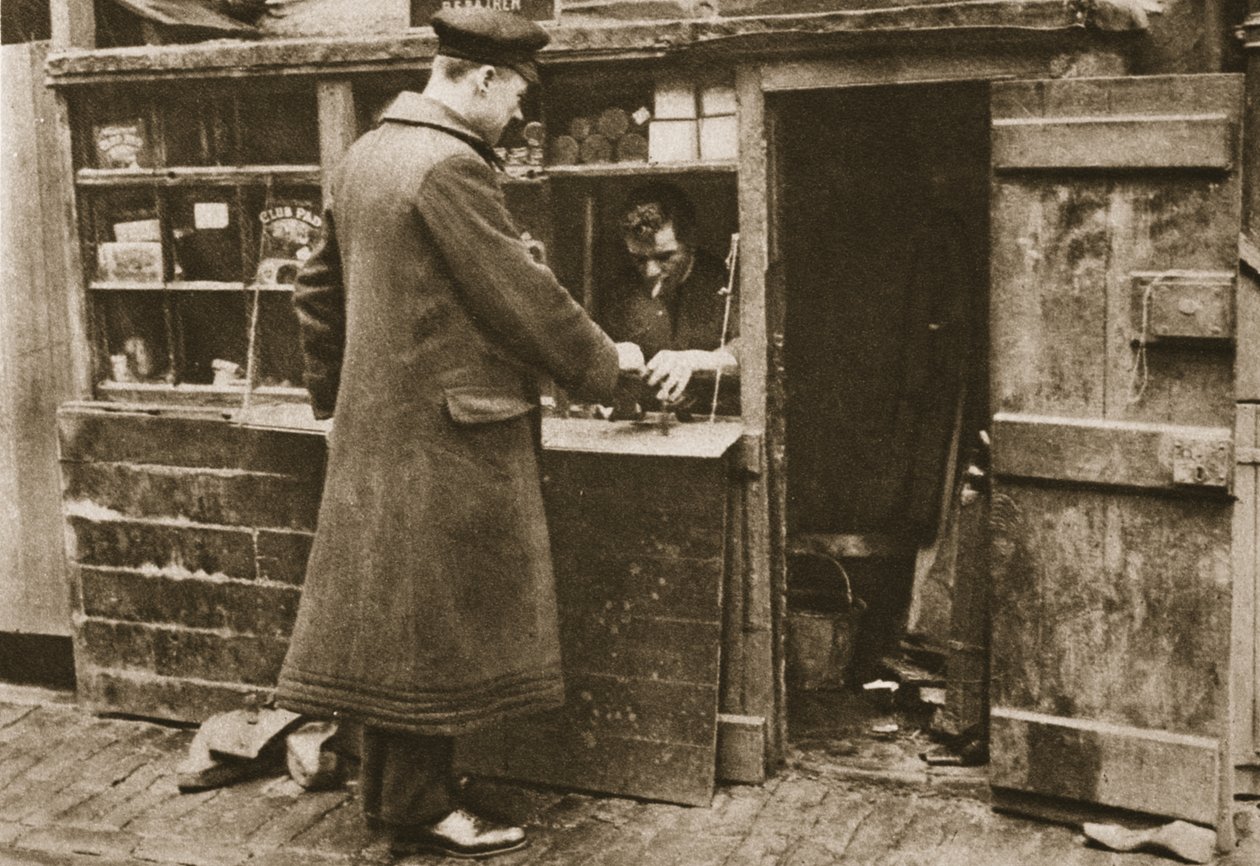 En skomakare, etablerad i en provisorisk monter i en kullerstensbelagd Mayfair-mew, tar in stövlar från en chaufför, från Wonderful London, publicerad 1926-27 (fotogravyr) av English Photographer