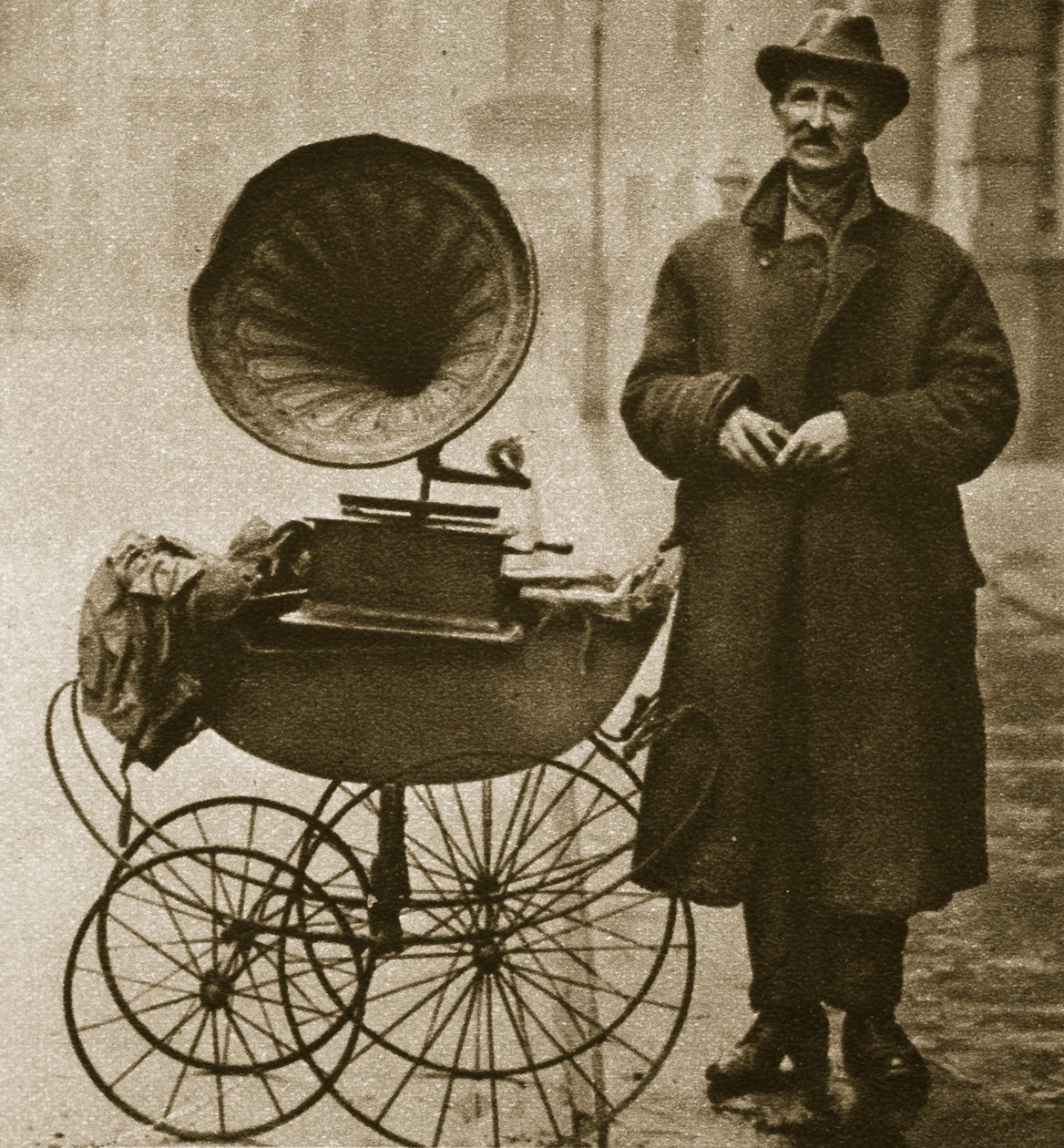 En gatuhandlare underhåller med en grammofon, transporterad i en barnvagn (sepiafoto) av English Photographer