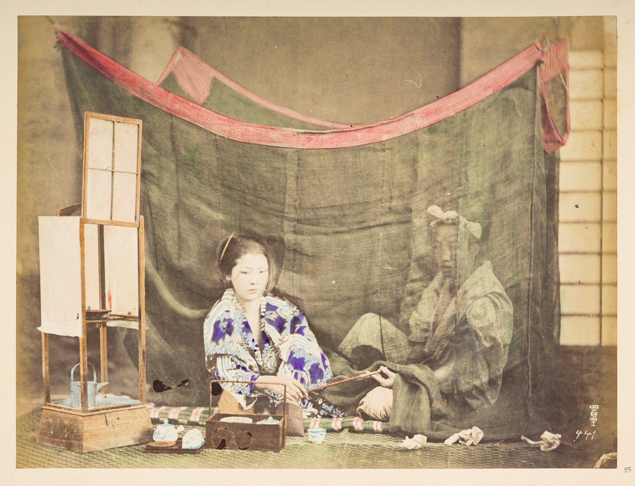 Japanskt par på sin fritid, Studiotablå av en ung japansk kvinna, sittande med tekokningshinder runt sig och räcker en pipa till en mansfigur som sitter bakom henne, skyddad av ett linnemyggnät,   Fotograf: Okänd  Lucas samling: av English Photographer