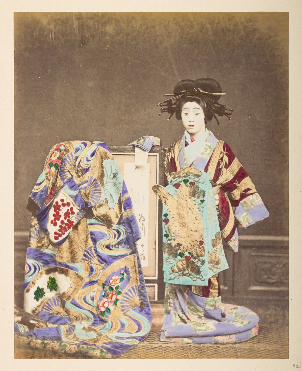 Japansk kvinna i traditionell klädsel, ] Stående studioporträtt i full längd av en kvinna som bär en utarbetad kostym och frisyr, med en annan dräkt draperad över ramen bredvid henne,  Fotograf: Okänd  Lucas Collection: Fotografisk inspelning av w av English Photographer