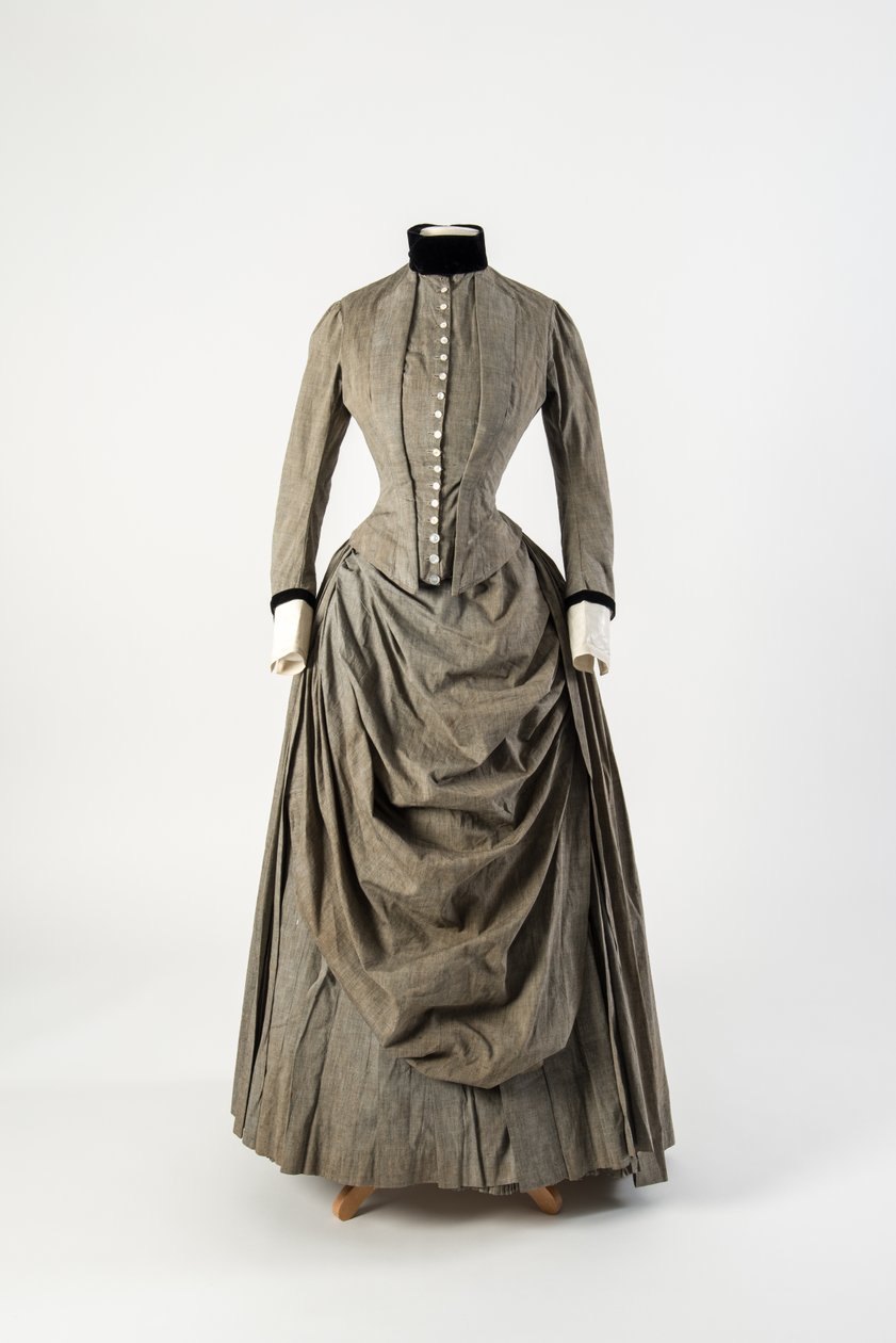 Grå bomullsklänning med draperat förkläde framtill och svart sammetskant vid krage och ärmslut, sent 1880-tal (bomull) av English School