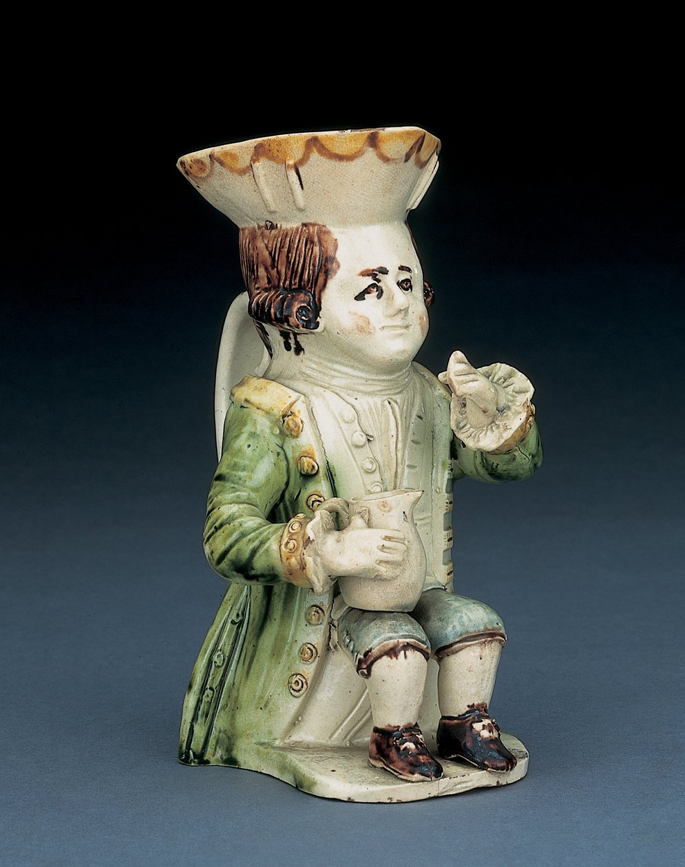 Toper toby-kanna, hans hatt med brun och gul bågad kant, hans inskurna bruna hår i kö och med en vit rosett sittande med en balusterkanna på knäet, ca 1770 av English School