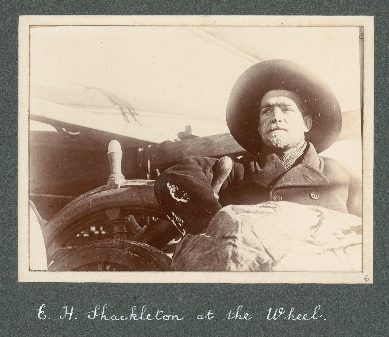 E H Shackleton står vid hjulet på "Discovery" (1901) Från album av Sir Ernest Henry Shackleton med titeln National Antarctic Expedition (1901-1903) av Ernest Henry Shackleton