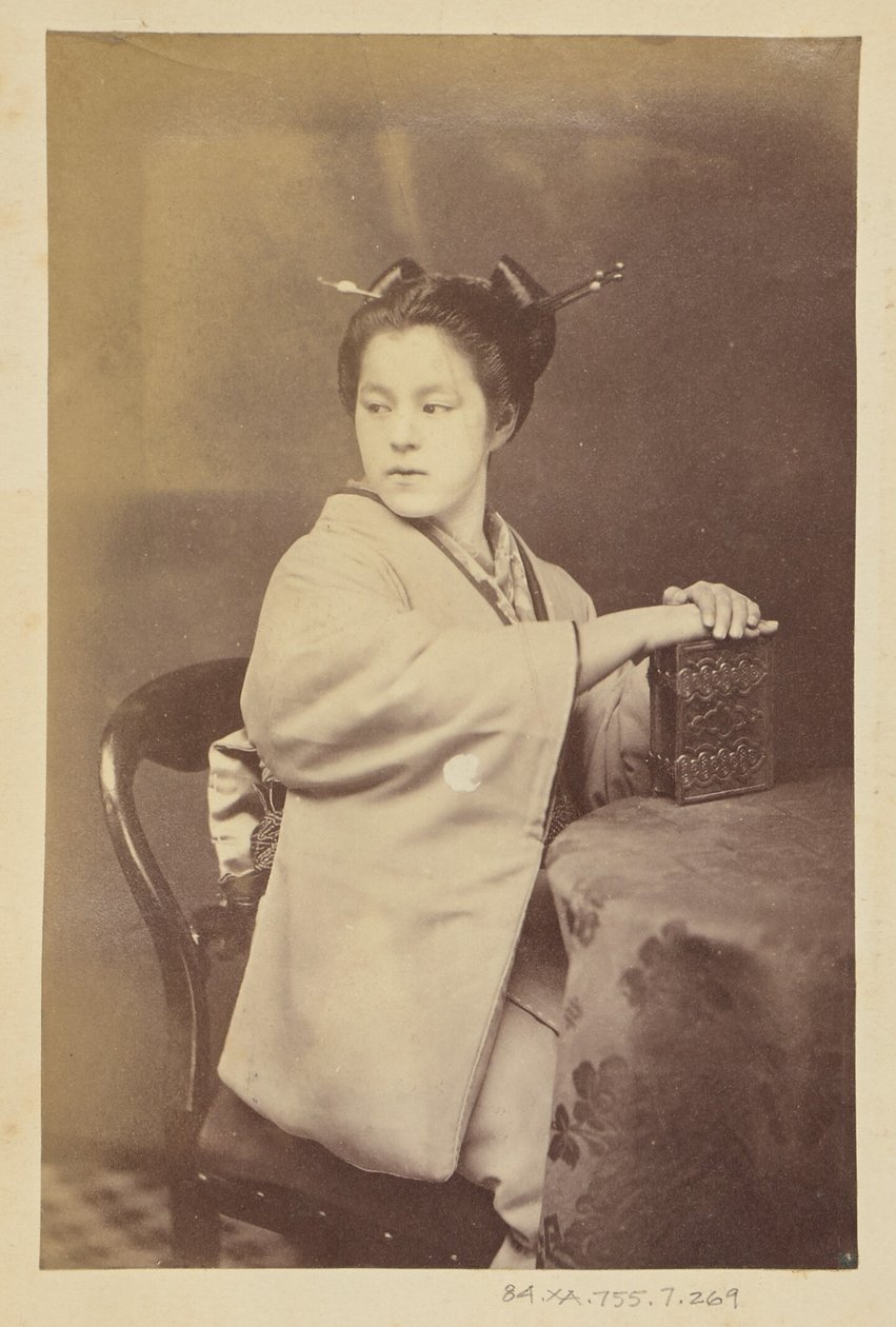 [Sittande japansk kvinna med ett album med cartes-de-visite vid ett bord] av Felice Beato