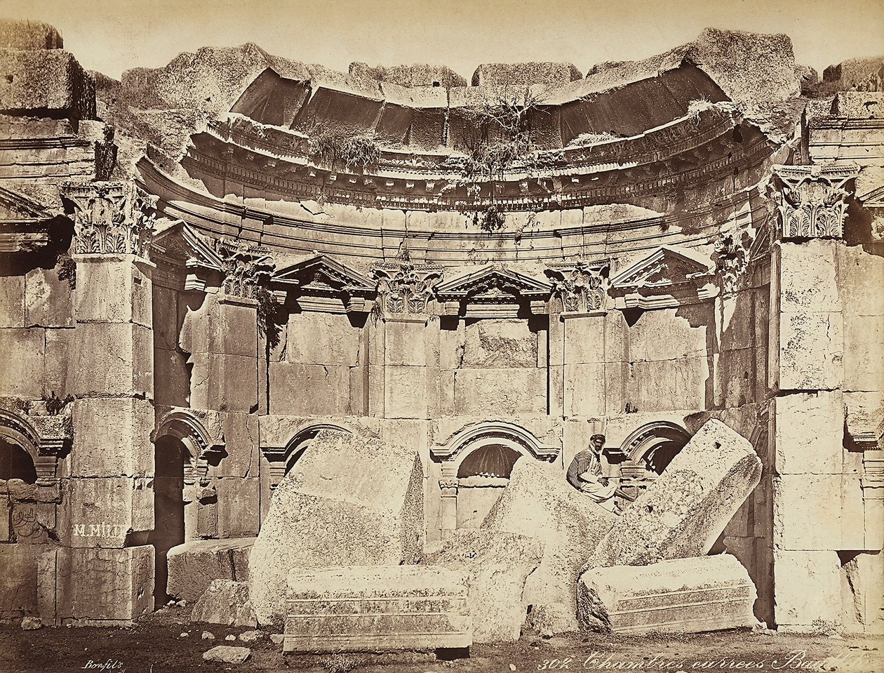 Detalj av de så kallade "rummen" i den arkeologiska zonen Heliopolis eller Baalbek, forntida syrisk stad, nu Libanon. En man poserar, sittande på ruinerna av Félix Bonfils