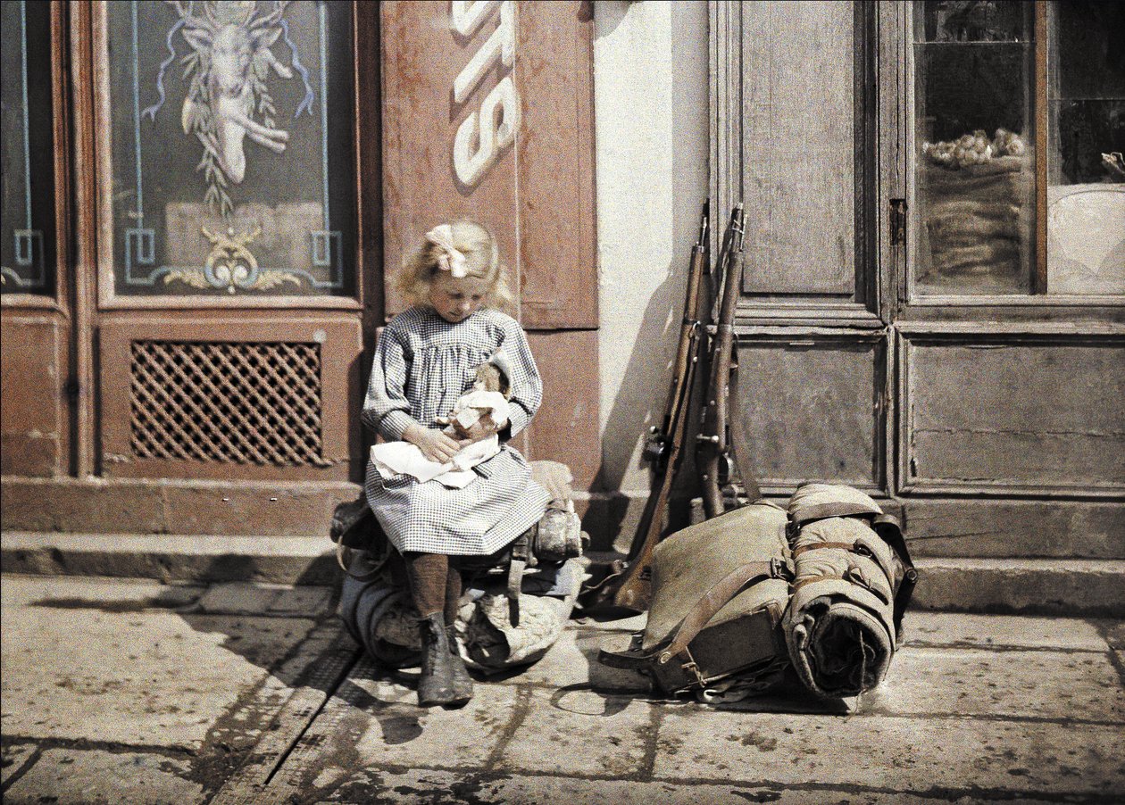 En liten flicka som leker med sin docka; två vapen och en ryggsäck ligger bredvid henne på marken, Reims, Marne, Frankrike, 1917 (autokrom) av Fernand Cuville