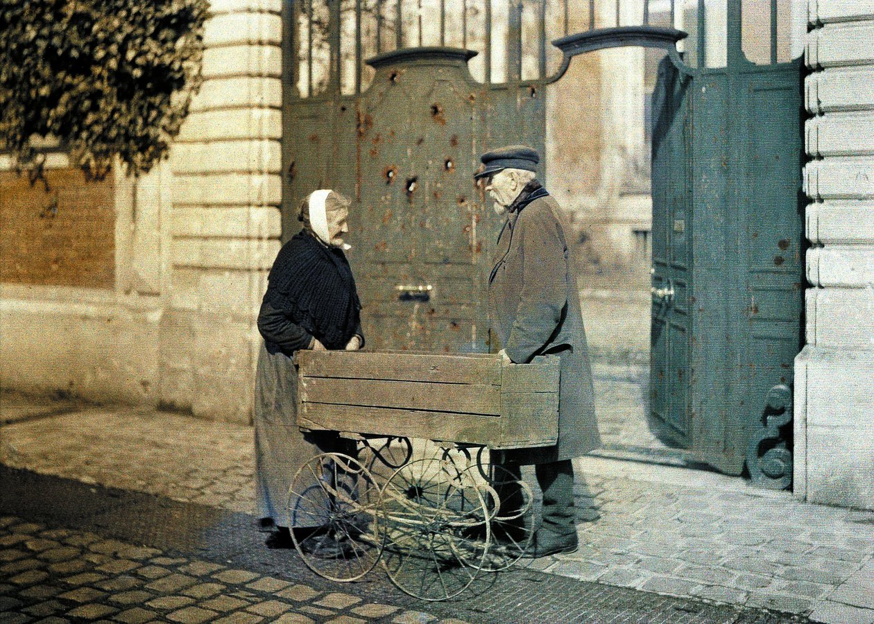 Två äldre medborgare i Reims, en gammal kvinna och herr Reiser, står framför en port med många skotthål, Reims, Marne, Frankrike, 1917 (autokrom) av Fernand Cuville