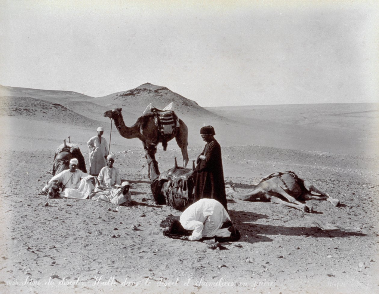 Egyptiska kamelerar under en paus i öknen. I förgrunden verkar två medlemmar i den lilla gruppen be av Félix Bonfils