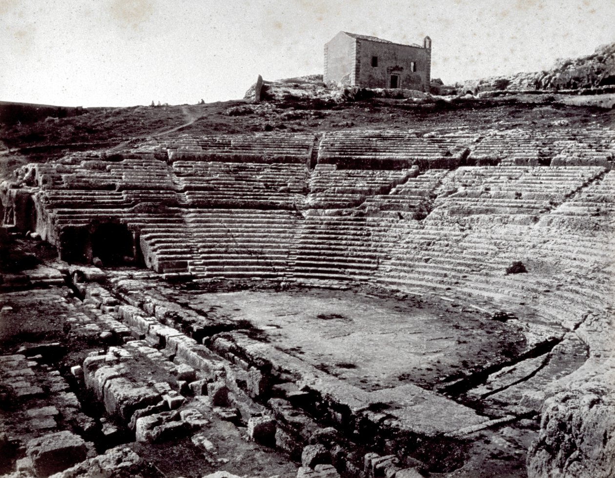 Resterna av den grekiska teatern i Siracusa i Neàpolls monumentala park. I förgrunden den halvcirkelformade orkestern och cavean av Giorgio Sommer