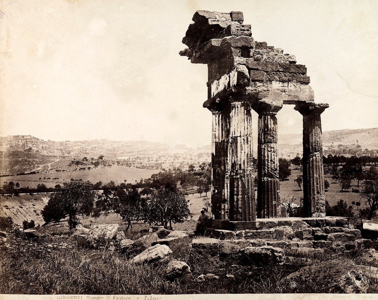 Vy över de återstående fyra kolumnerna som stöder en entablatur av Castor- och Polluxtemplet i Valle dei Templi, Agrigento. Ett panorama över staden syns i bakgrunden av Giorgio Sommer